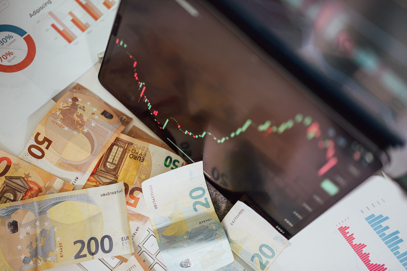 Billetes de euro junto a una pantalla con un gráfico de bolsa