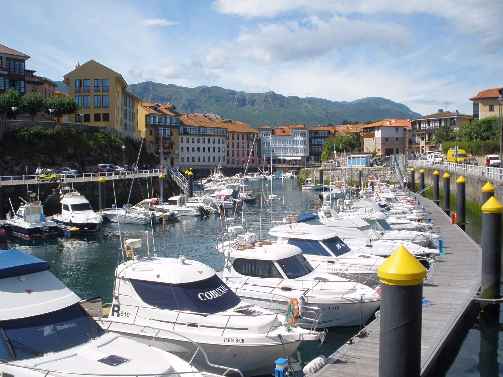 Puerto deportivo de Llanes (Asturias) con embarcaciones amarradas, casas tradicionales y montañas al fondo